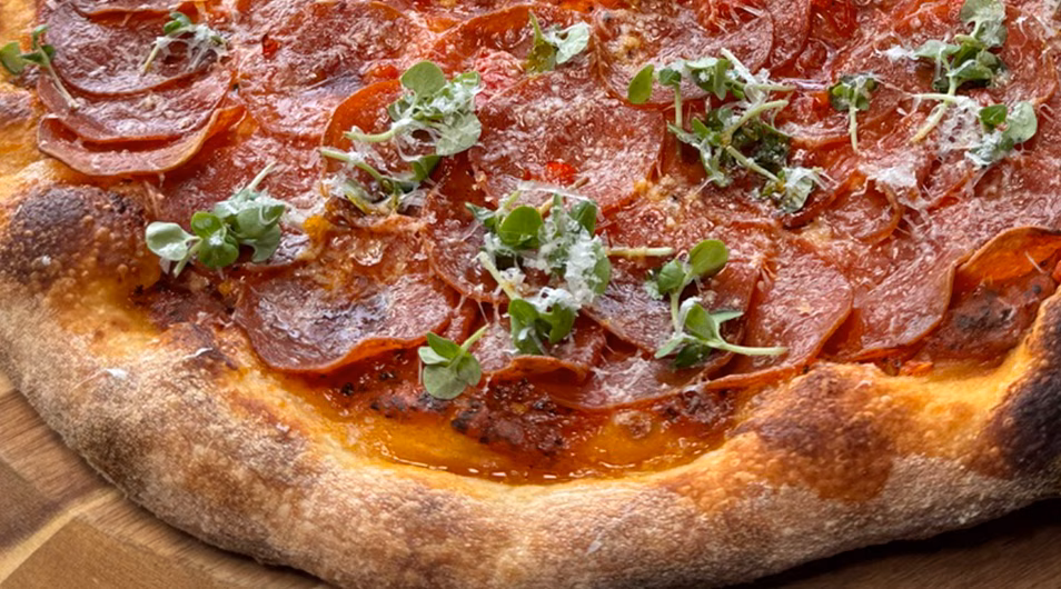 Close-up of a pepperoni pizza with microgreens and grated cheese.