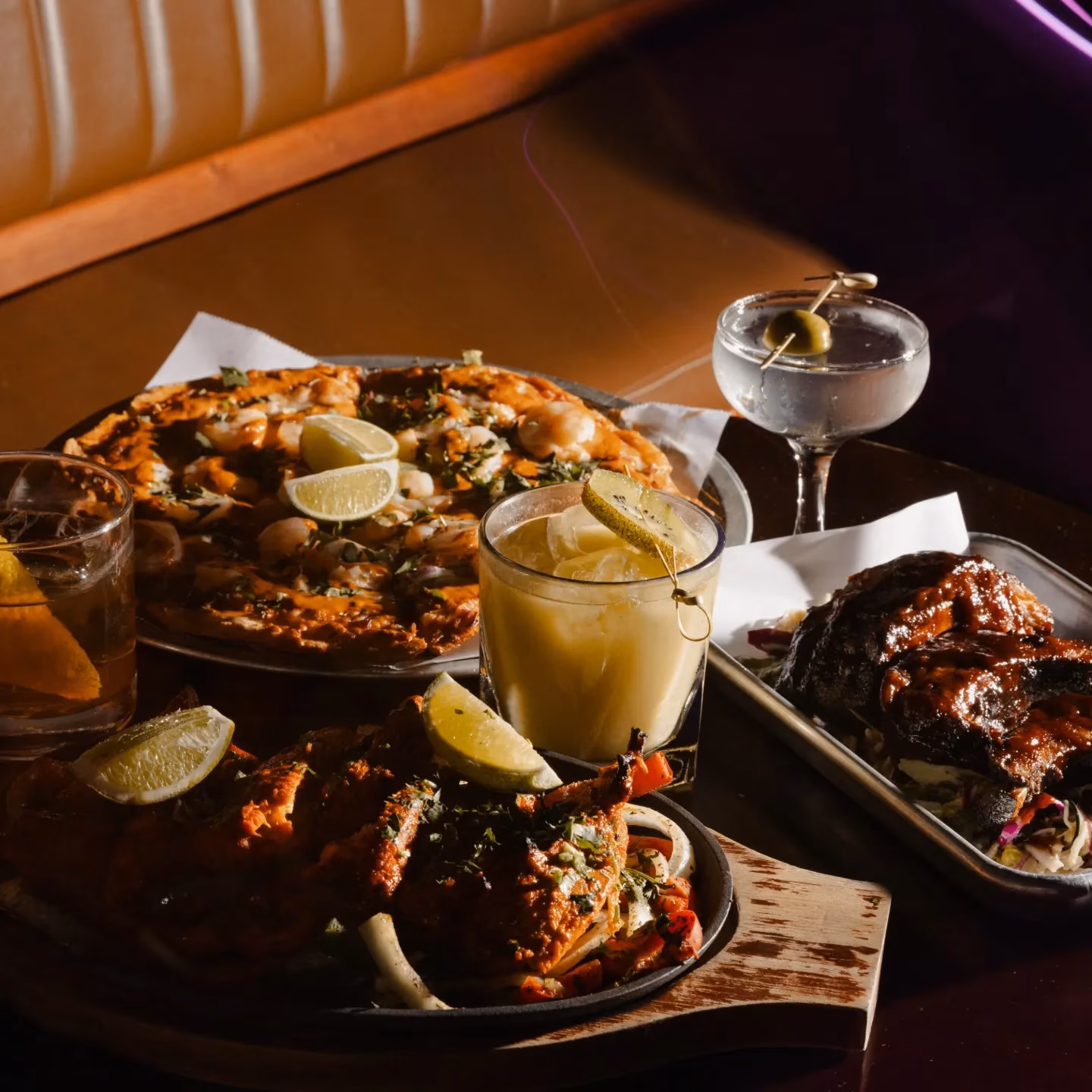 Pizza, ribs, chicken, and three cocktails on a table.