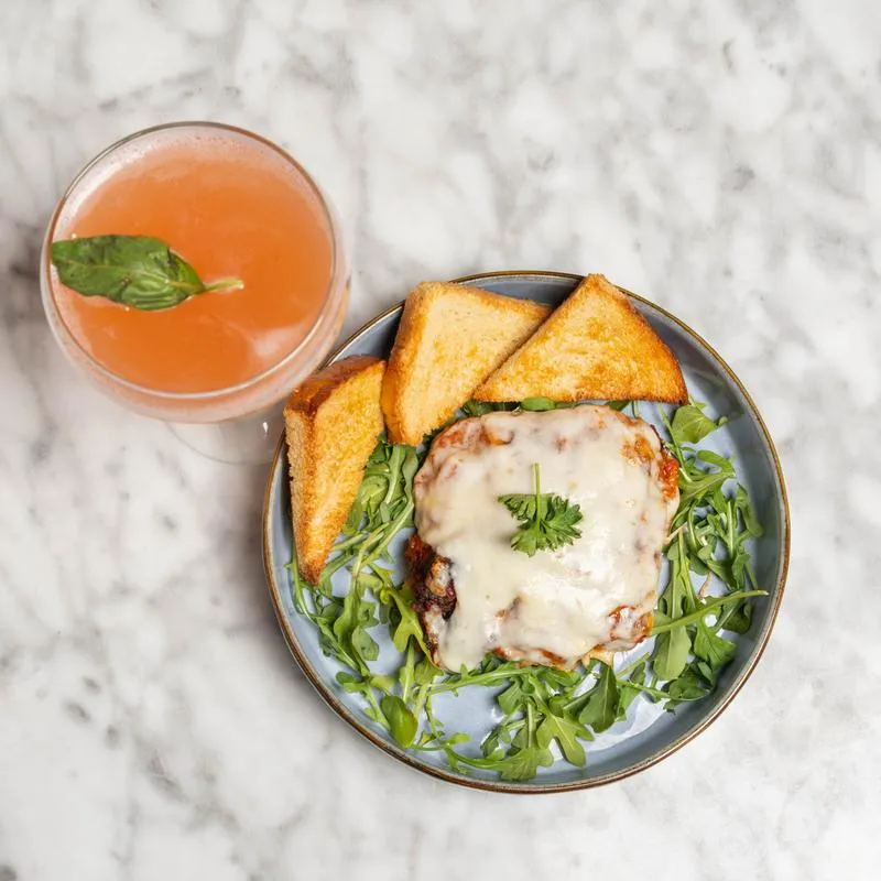 Cheesy dish on arugula with toasted bread and a pink drink.