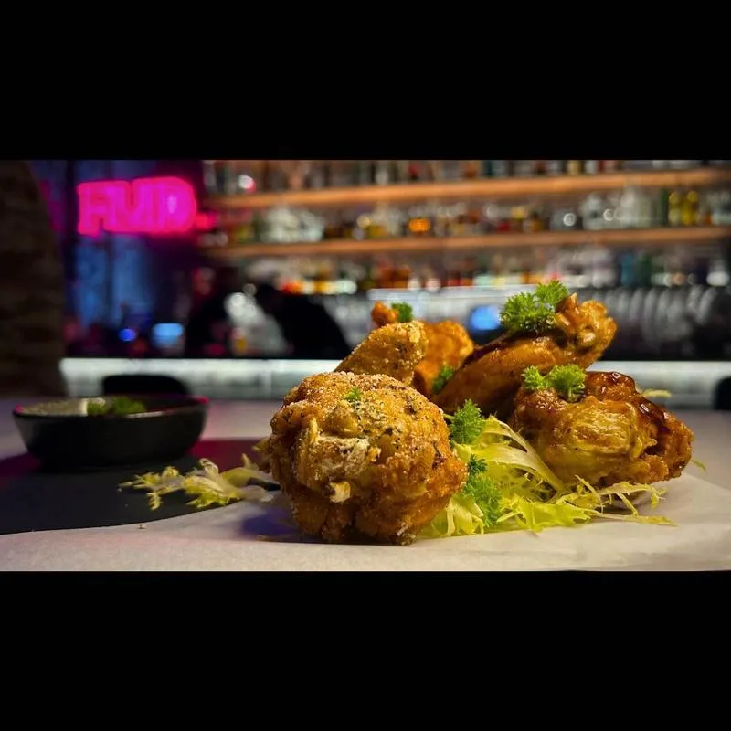 Fried chicken wings and a fried ball on a plate at a bar.