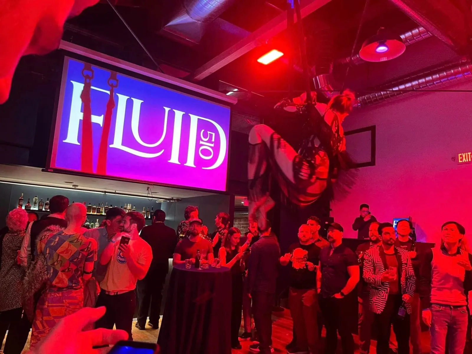 Indoor event with red lighting, 'FLUID 510' screen, and aerialist.