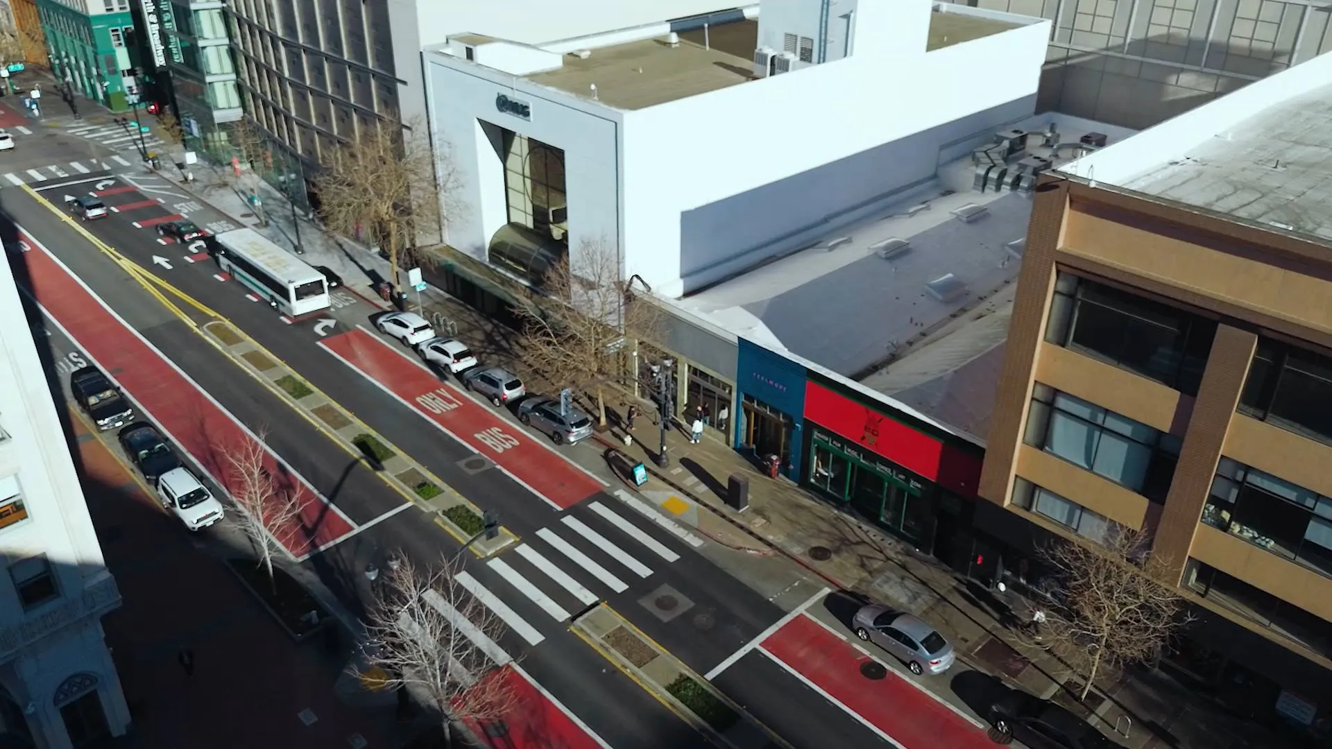 Aerial view of a city street with red bus lanes, vehicles, and buildings.