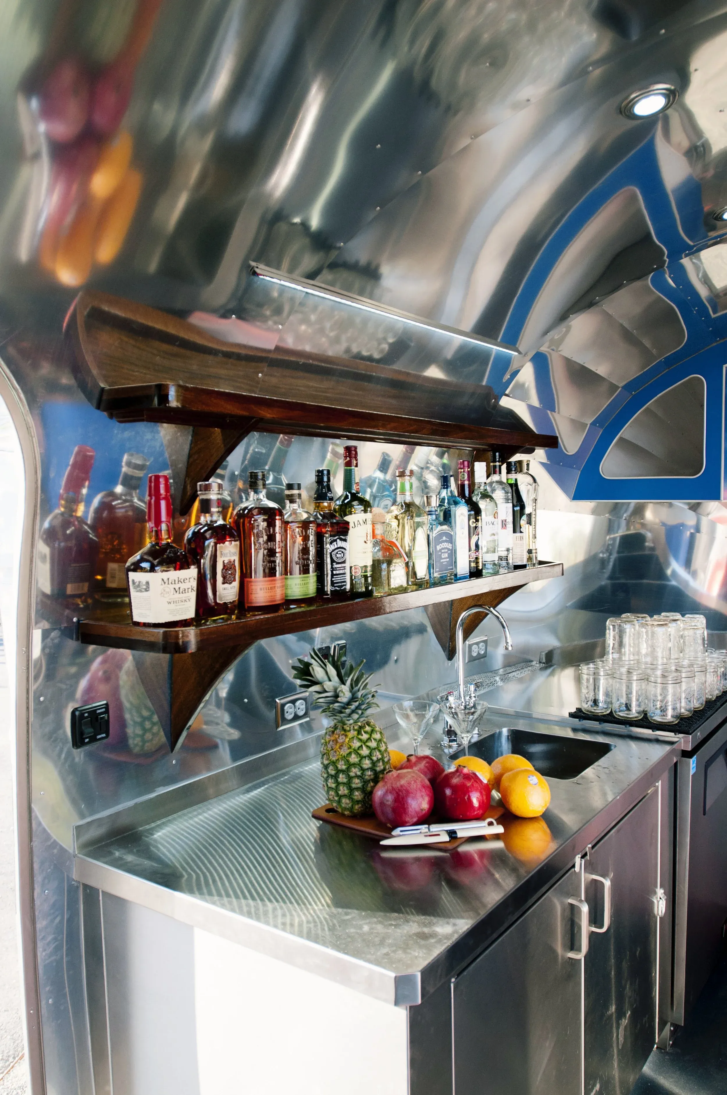 Metallic bar interior with liquor bottles, sink, fruit, and glass jars.