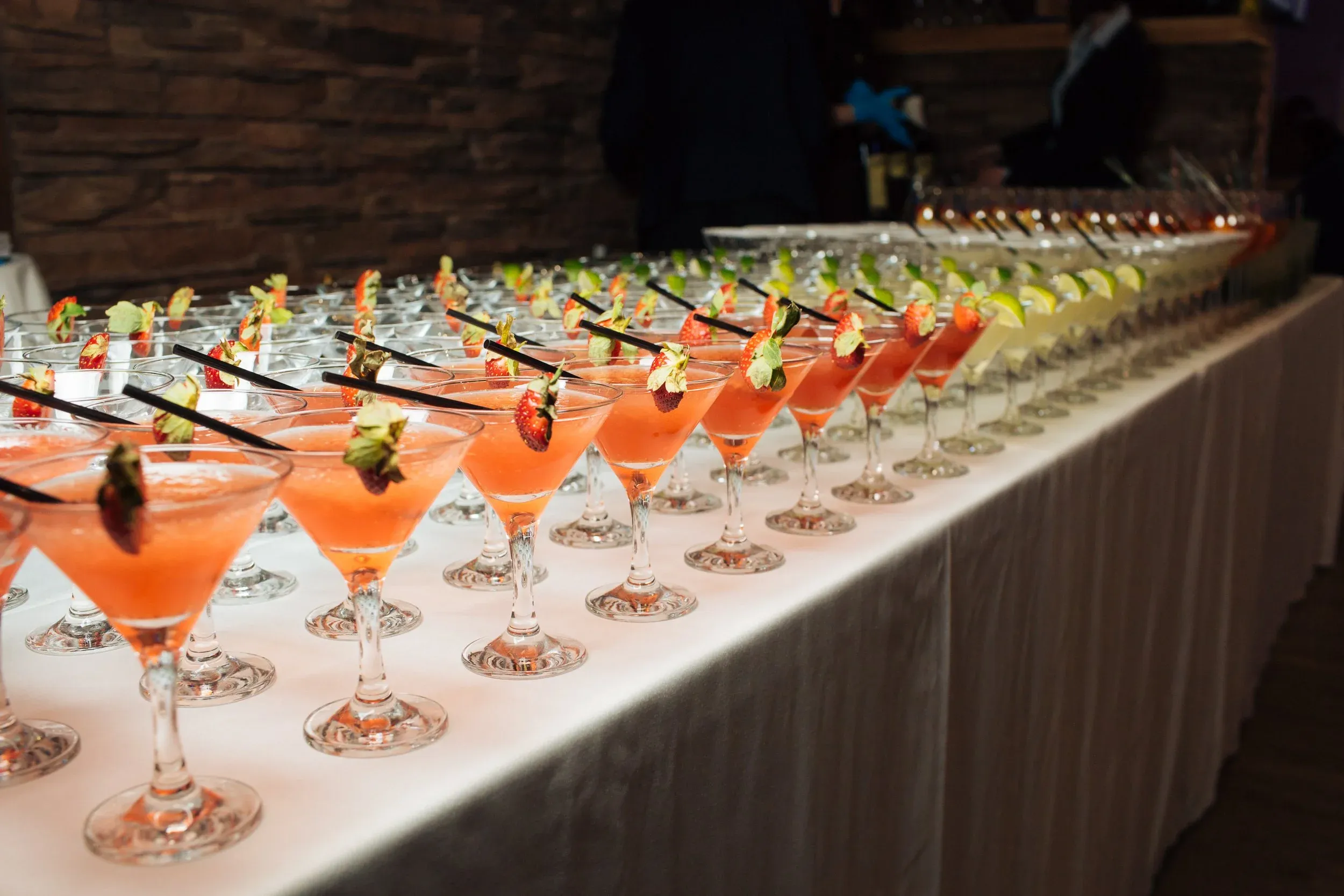 Numerous cocktails with strawberry and lime garnishes on a long table.