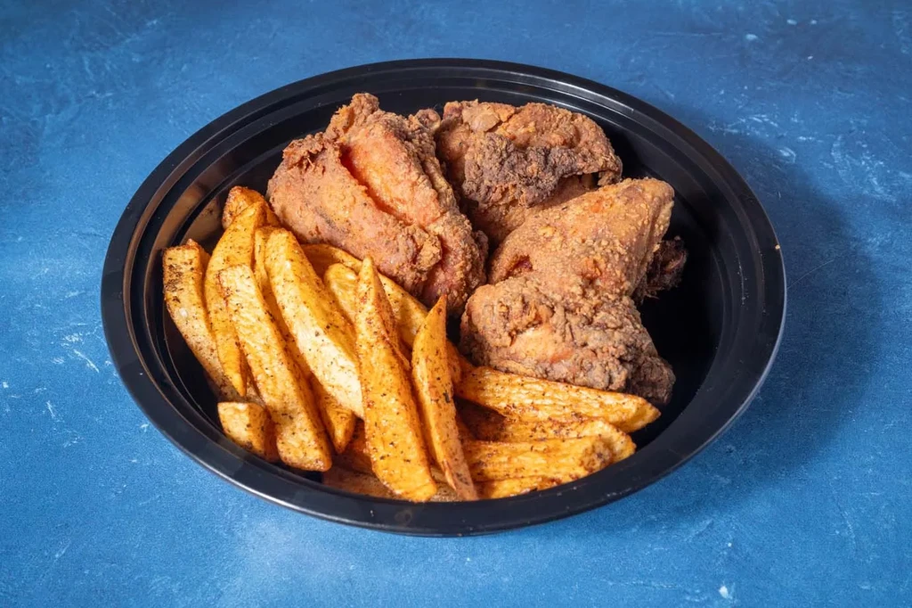 Fried chicken pieces and seasoned potato wedges in a black bowl.