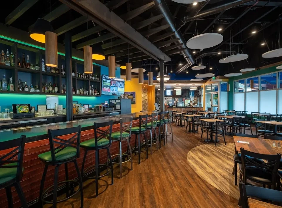 A brightly lit, empty bar and restaurant with wooden floors and tables.