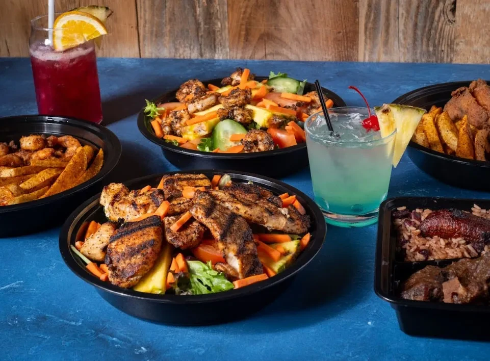 Takeout containers filled with chicken, shrimp, fries, rice, and cocktails.