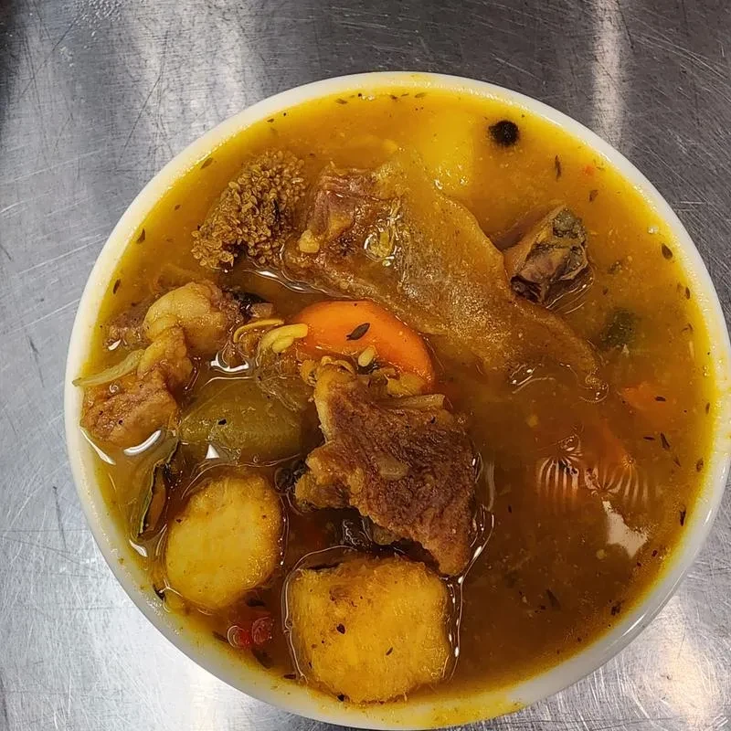 A bowl of yellow stew with meat, vegetables, and potatoes.
