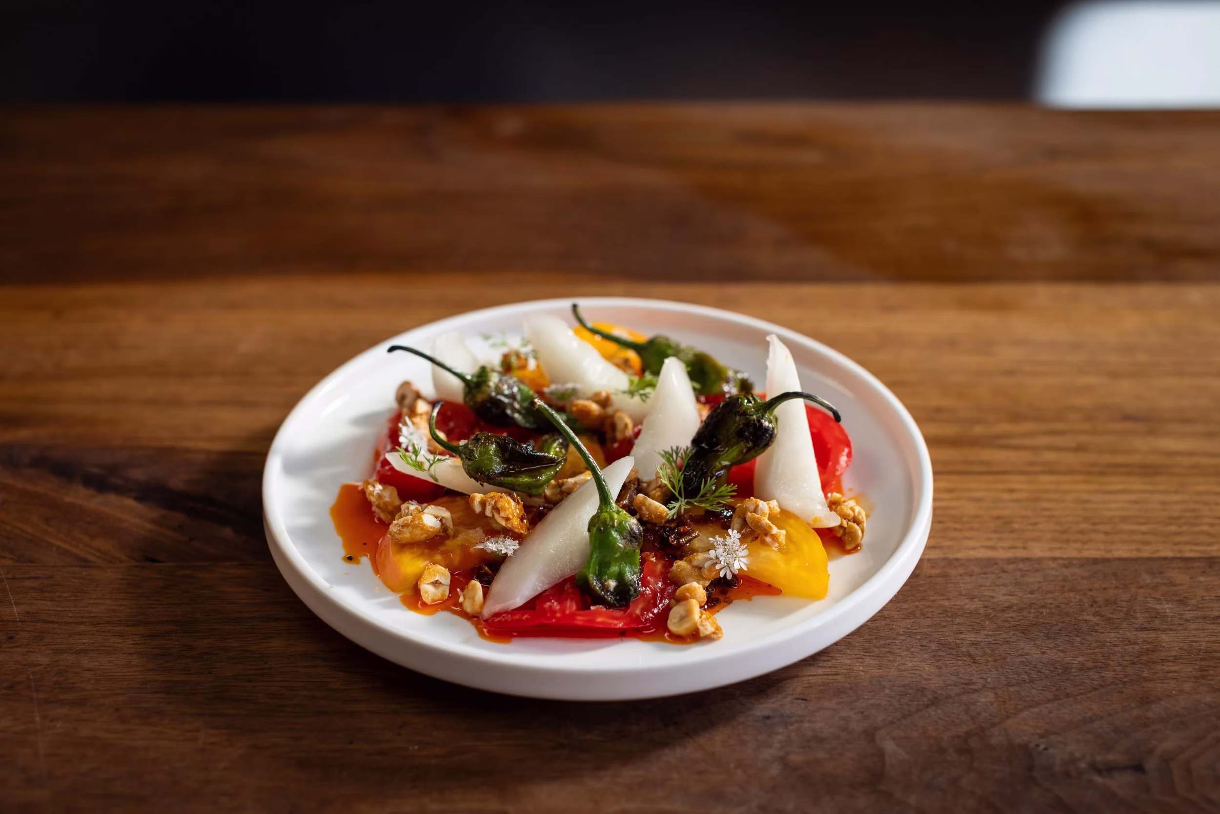 Plate of tomato salad with peppers, white vegetables, and nuts.