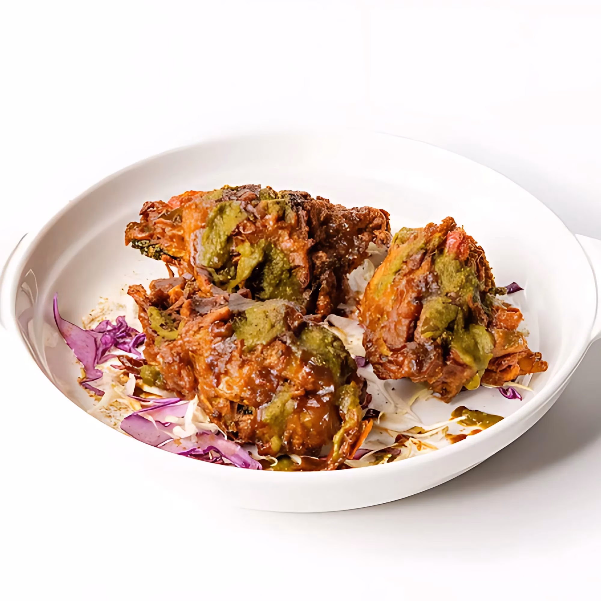 Fried fritters with green sauce on shredded cabbage in a white bowl.