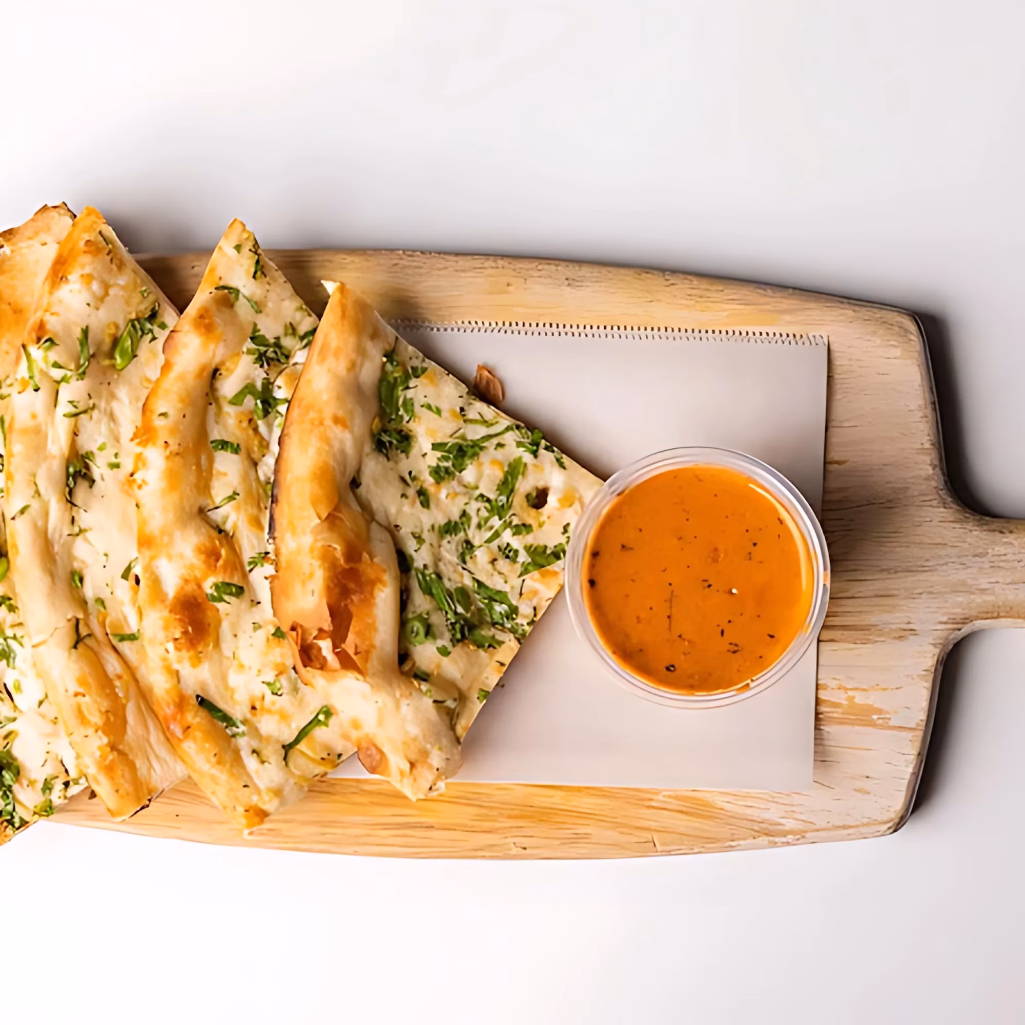 Triangular flatbread with herbs and orange dipping sauce on wood.