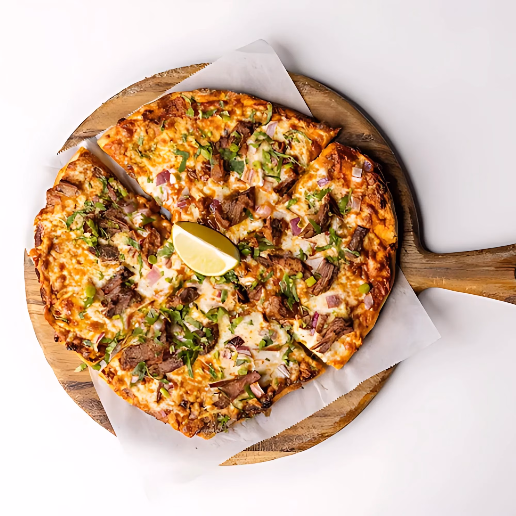 Pizza cut into slices with meat, red onion, herbs, and lime.