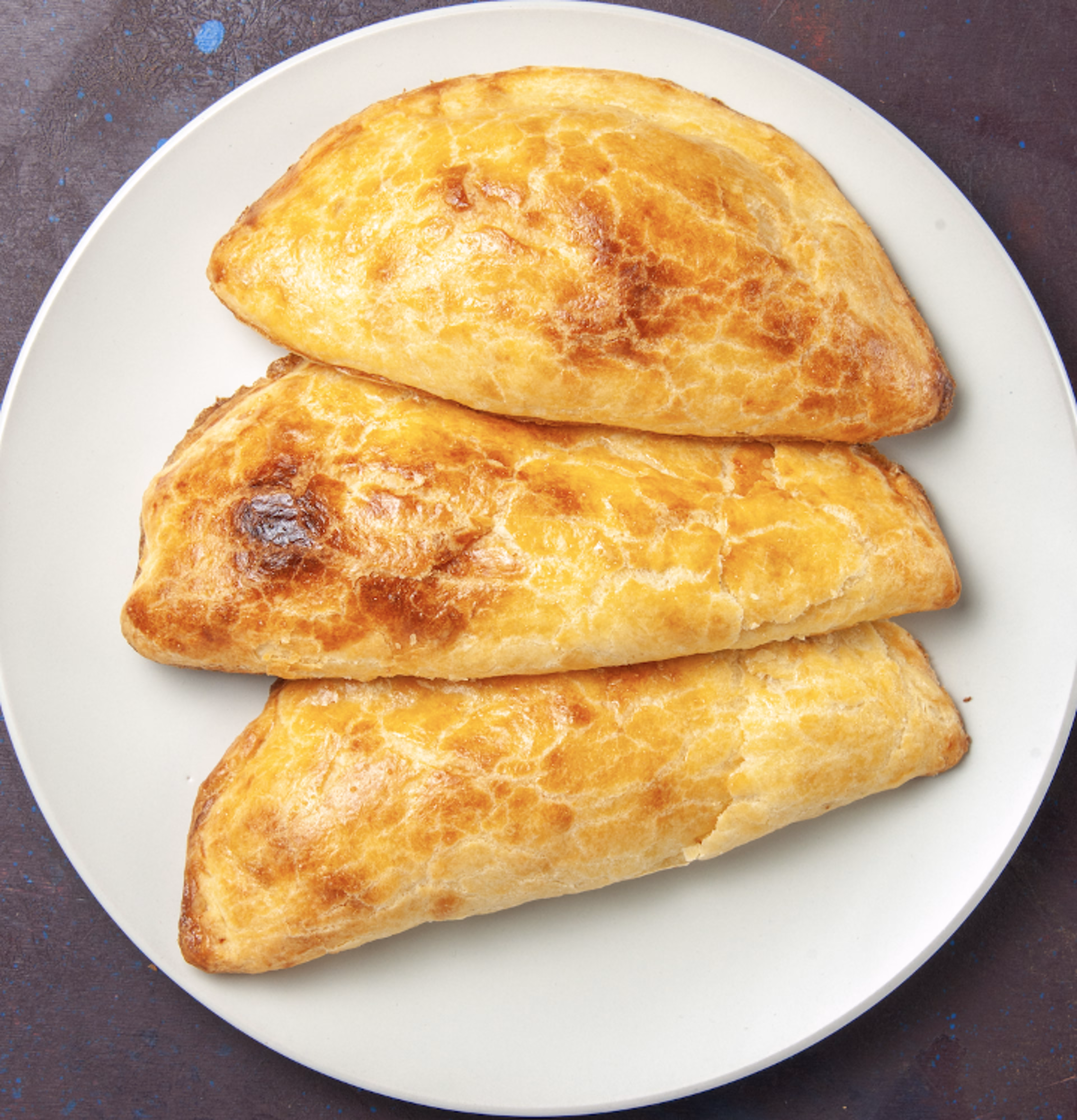 Three golden-brown baked pastries on a white plate.