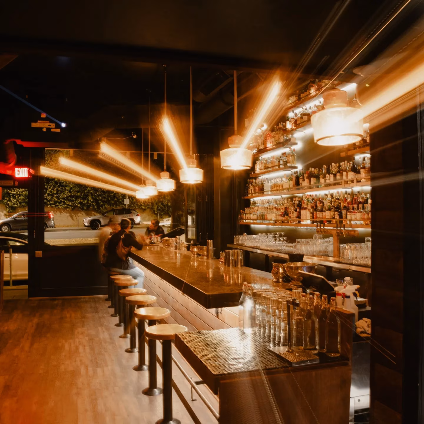 Bar interior at night with patrons, liquor shelves, and streaky lights.