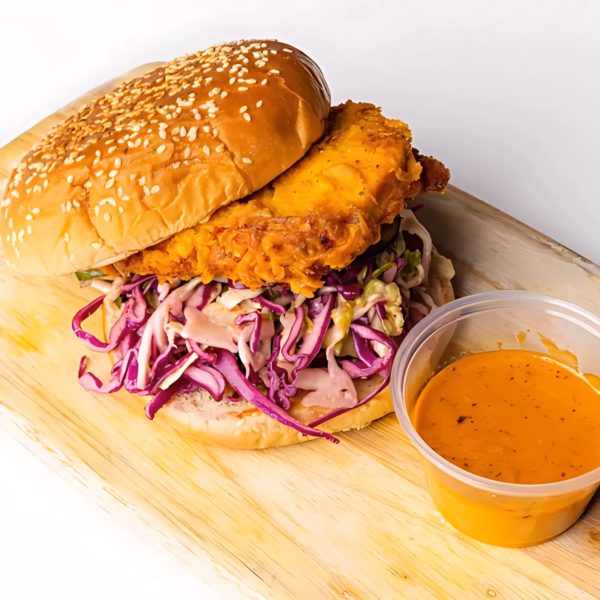 Fried chicken sandwich with coleslaw and orange sauce on a wooden board.