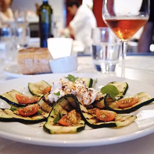 A restaurant plate of grilled zucchini, cherry tomatoes, and fresh cheese.