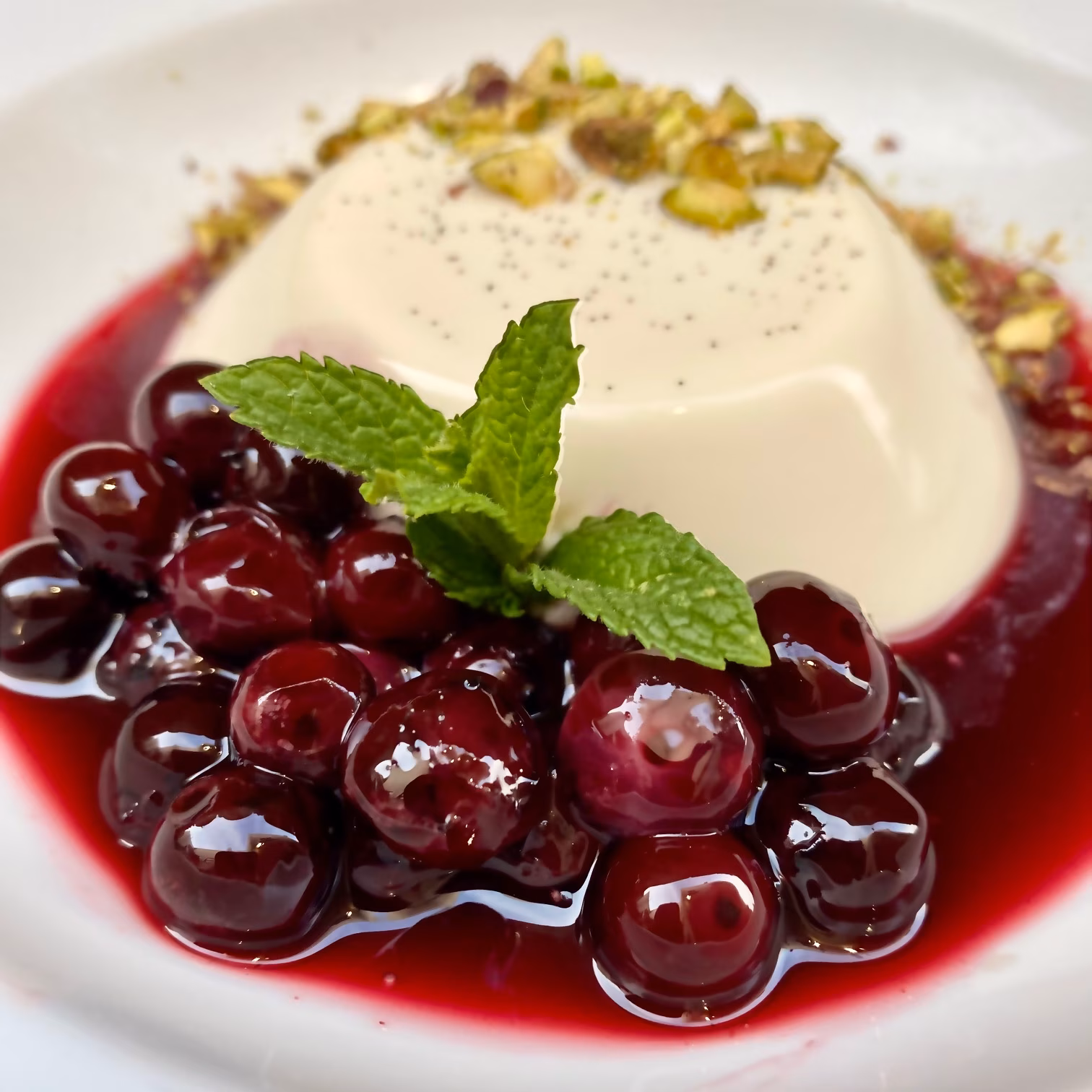 White dome dessert with cherries, mint, pistachios, and red sauce.