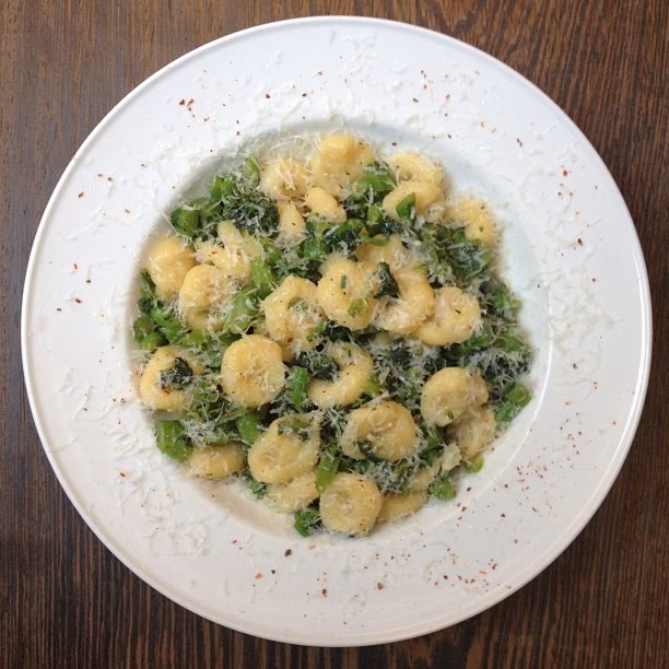 Gnocchi with green vegetables and grated cheese on a white plate.