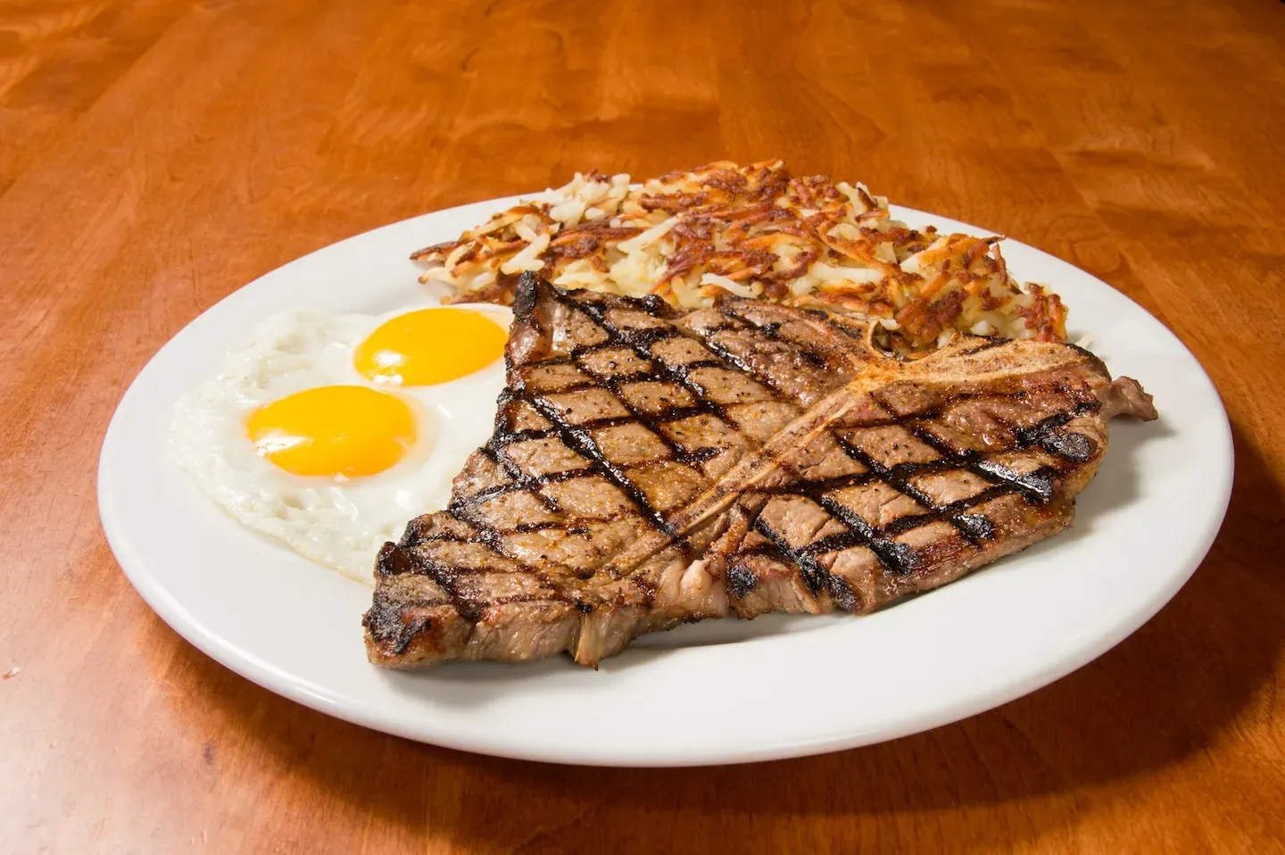 Grilled T-bone steak, two fried eggs, and hash browns.