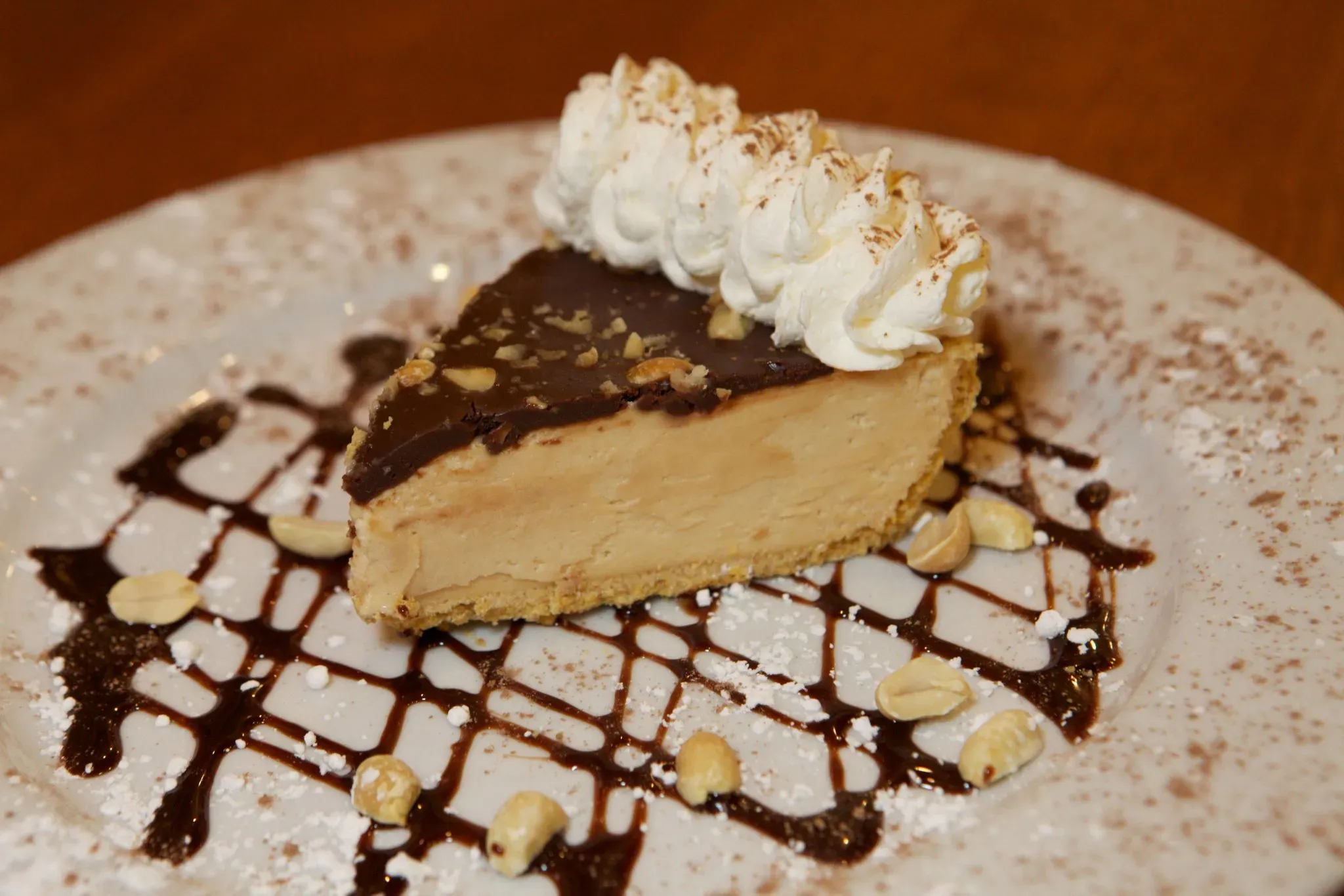 Slice of peanut butter pie with chocolate, whipped cream, and peanuts.