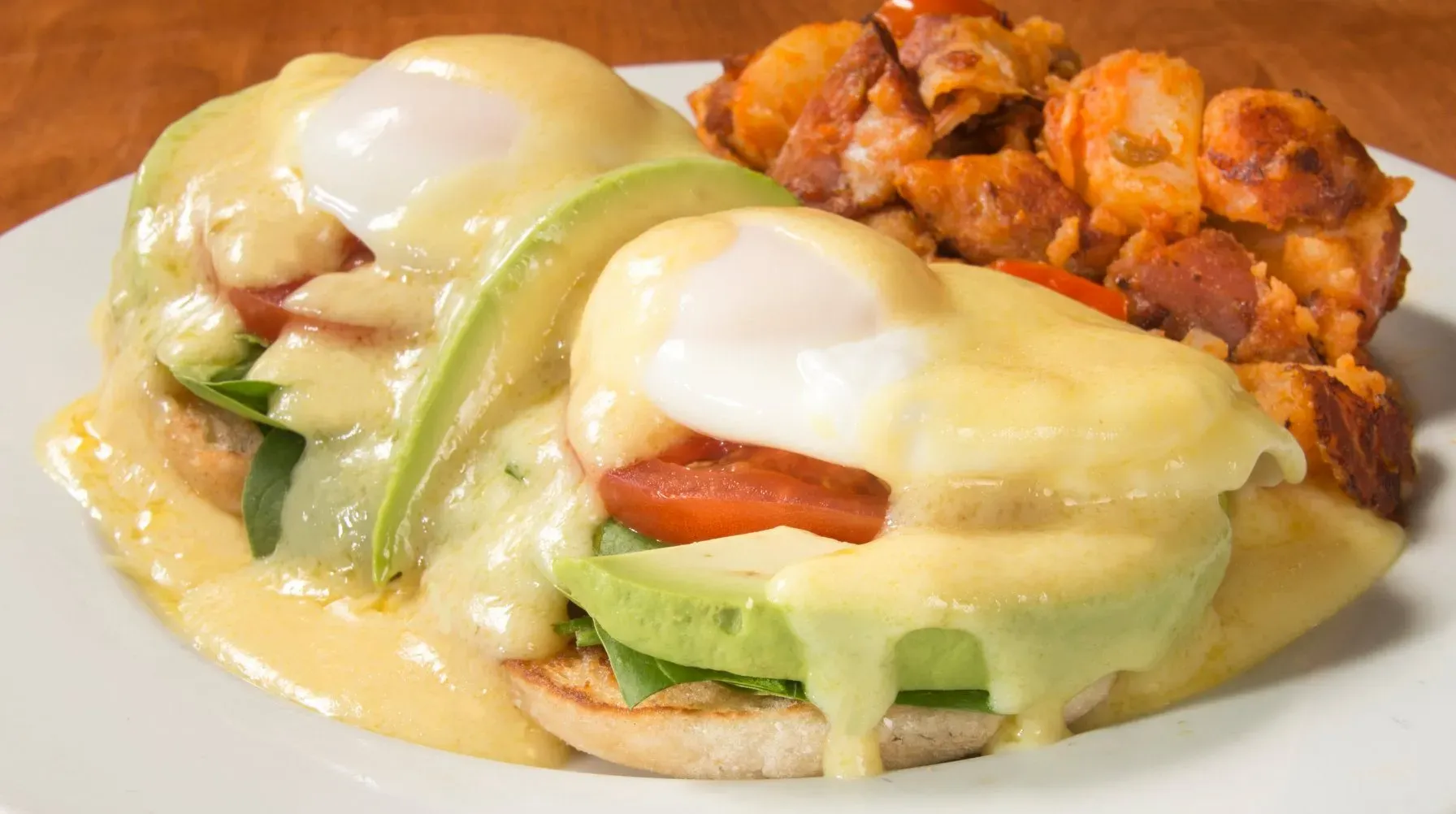 Two Eggs Benedict with avocado, tomato, spinach, hollandaise, and breakfast potatoes.