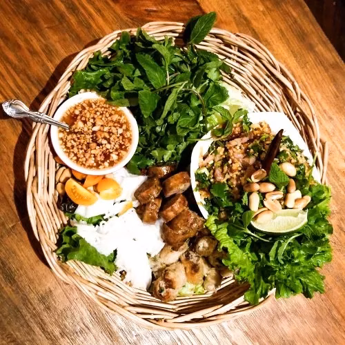 Vietnamese grilled meat, salad, herbs, noodles, and dipping sauce on a basket.