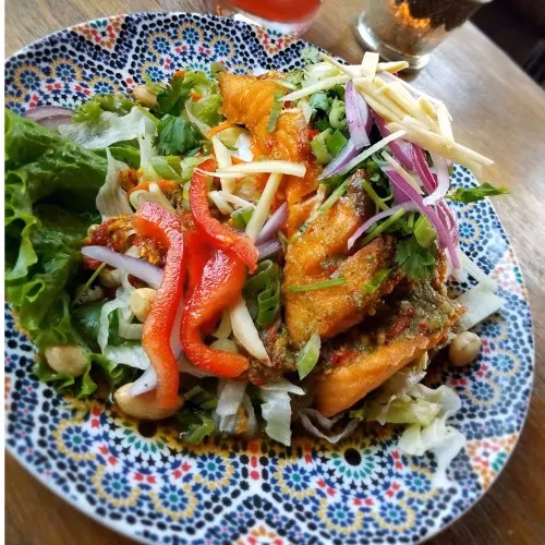 Crispy fish, mixed salad, red peppers on a colorful patterned plate.