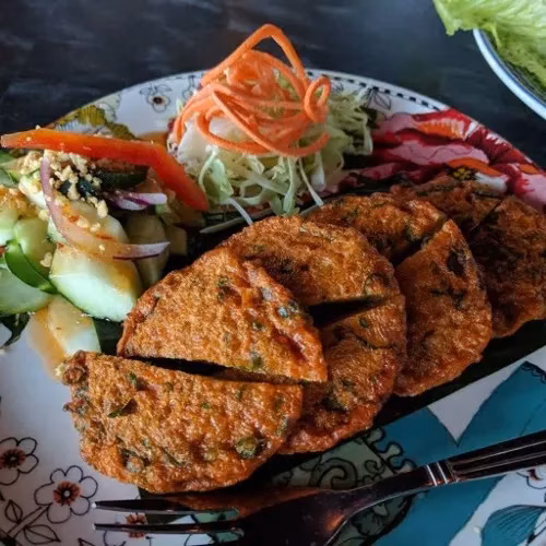 Golden fried patties served with cucumber salad and shredded vegetable garnish.