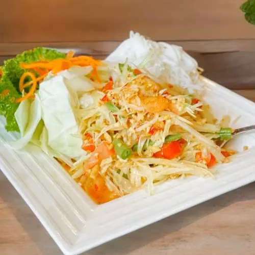 A plate of papaya salad with fresh vegetables and rice noodles.