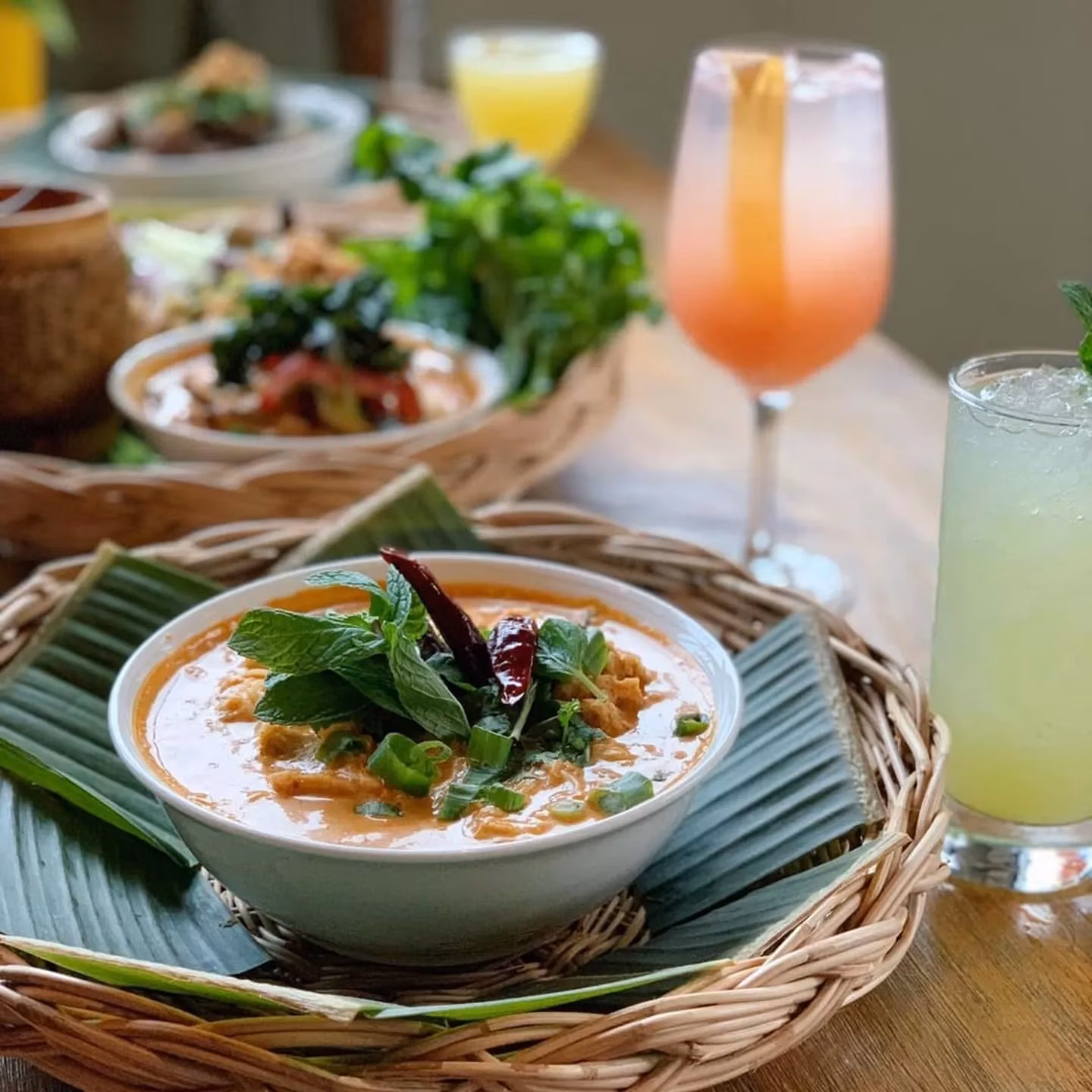 Bowl of reddish-orange curry with mint and chilies on a woven tray.