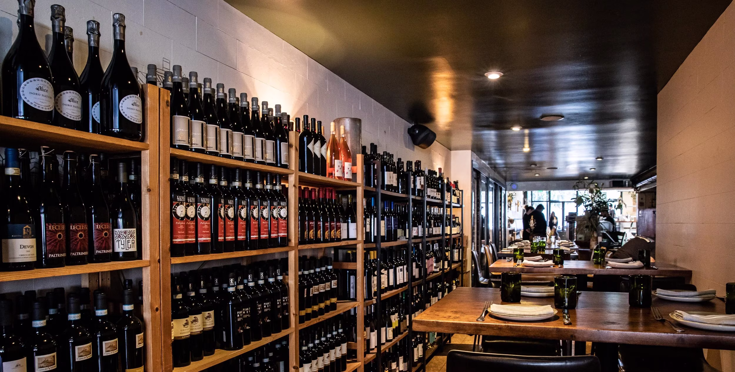 Dining room with wooden shelves full of wine bottles and set tables.