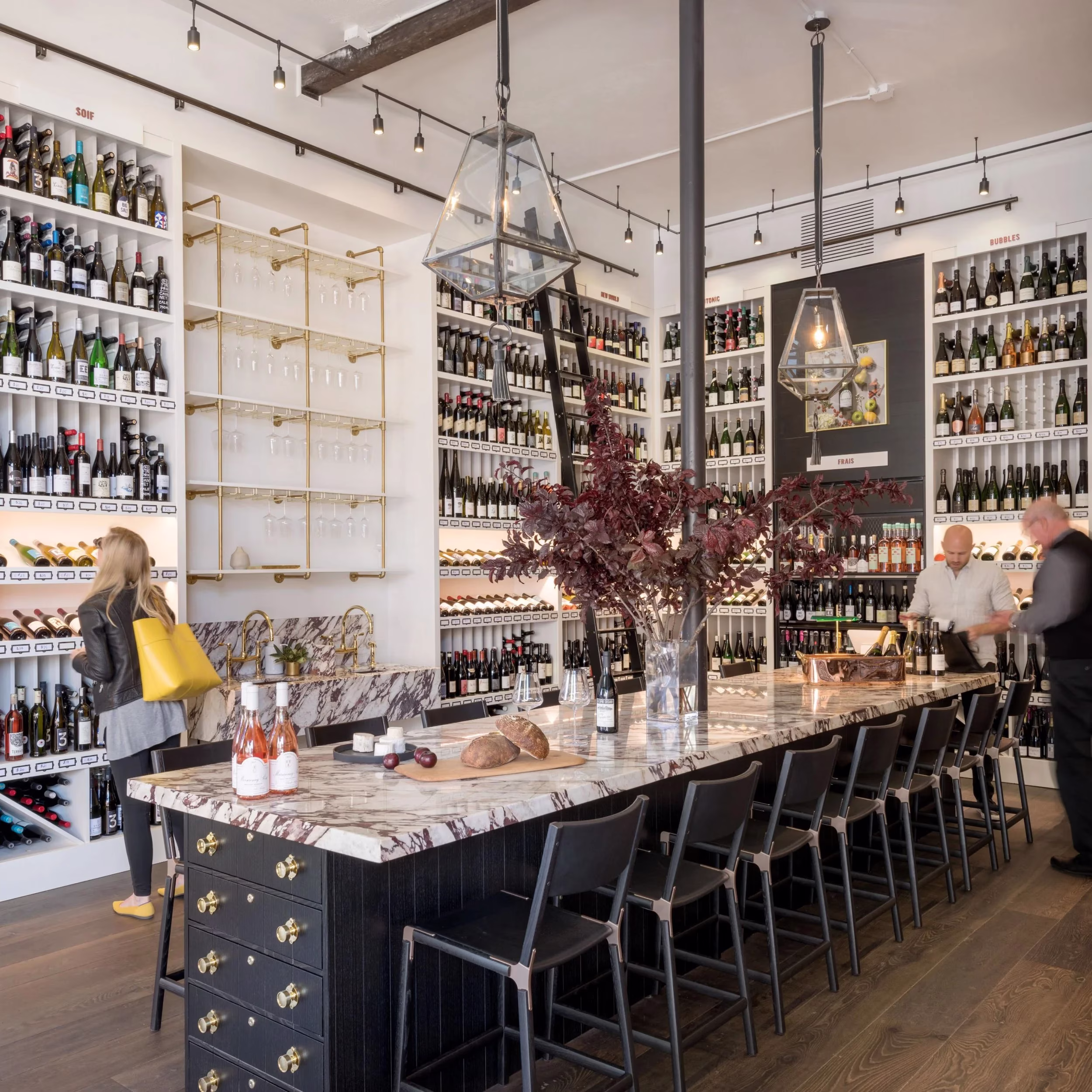 Wine shop interior with shelves of bottles, a long bar, and people.