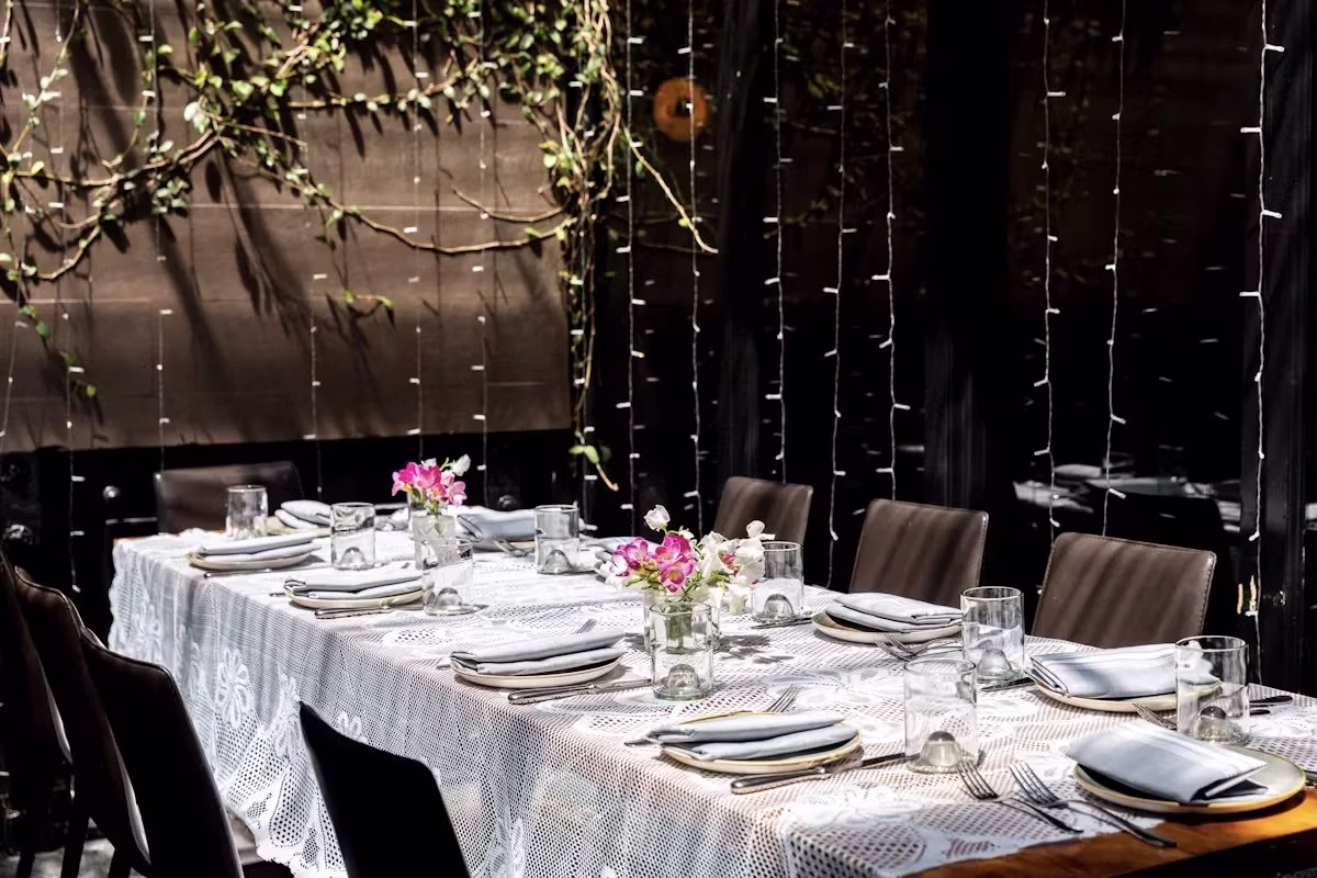 Long dining table set with white lace, flowers, and string lights.