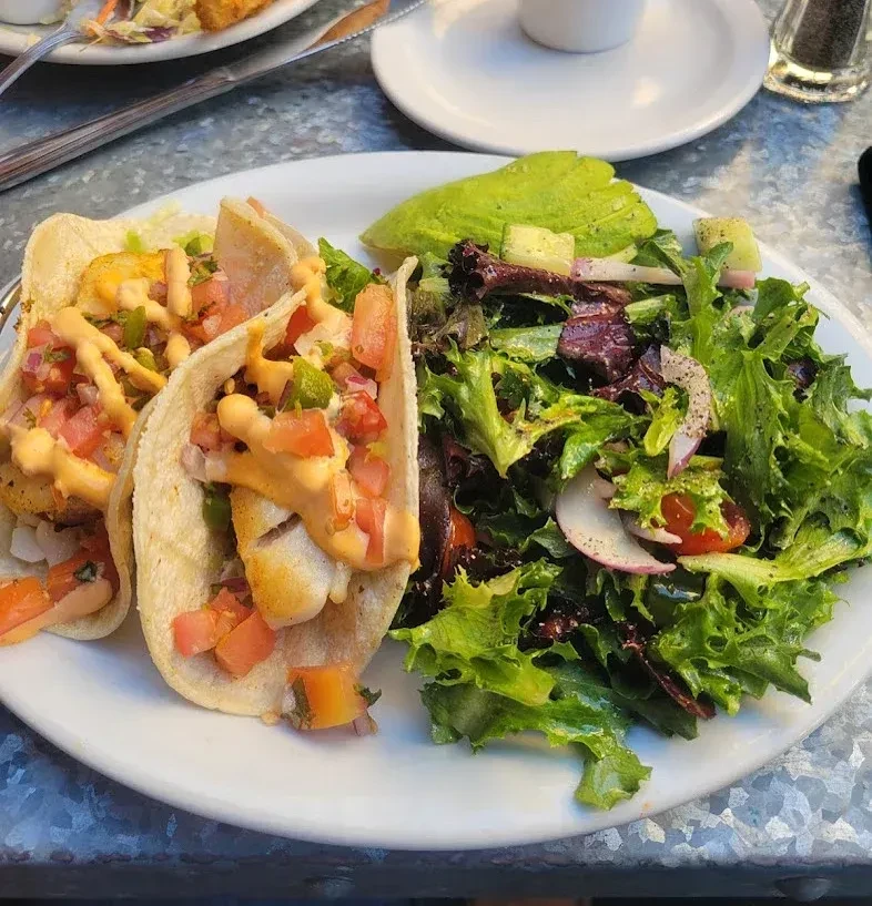 A plate with two fish tacos, a side salad, and a slice of avocado.
