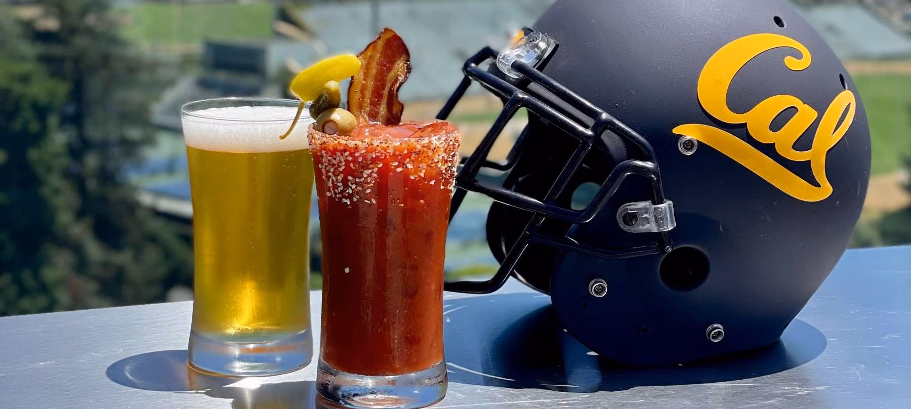 Beer, Bloody Mary, and Cal football helmet on an outdoor table.