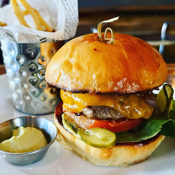 Cheeseburger with fries and dipping sauce on a white plate.