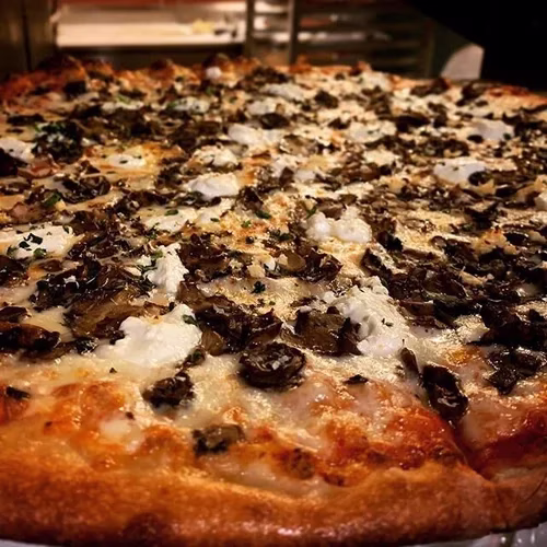 Whole pizza with dark mushrooms, white cheese dollops, and herbs.
