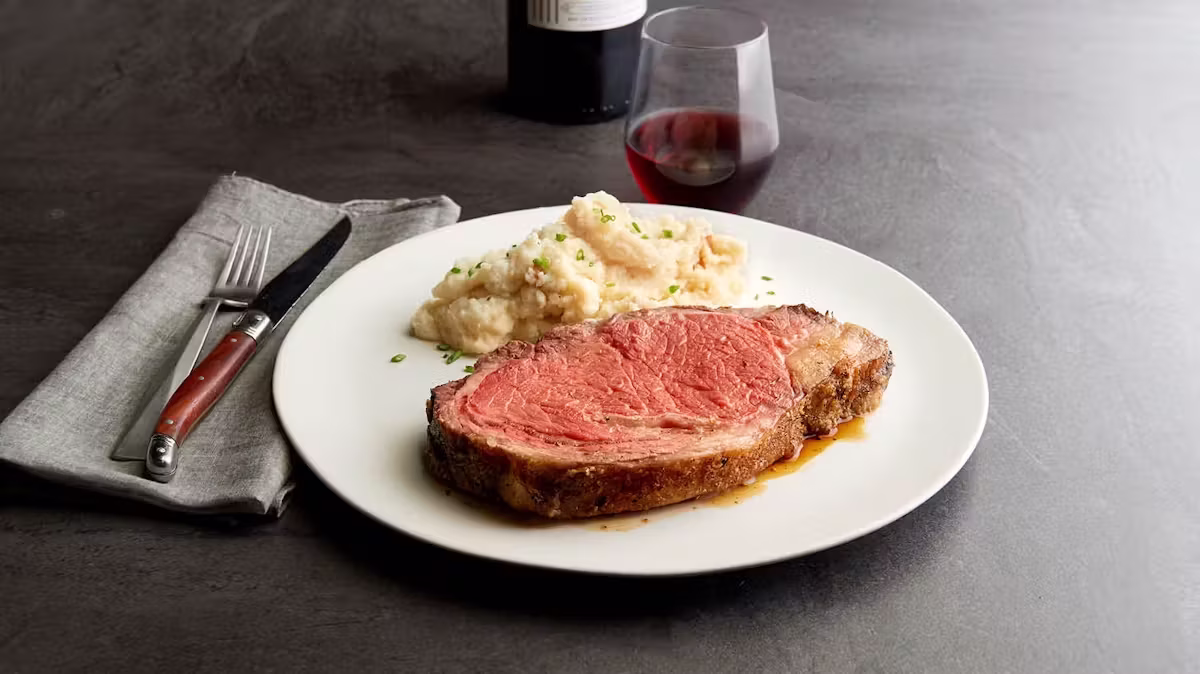 Plate with medium-rare prime rib, mashed potatoes, and red wine.