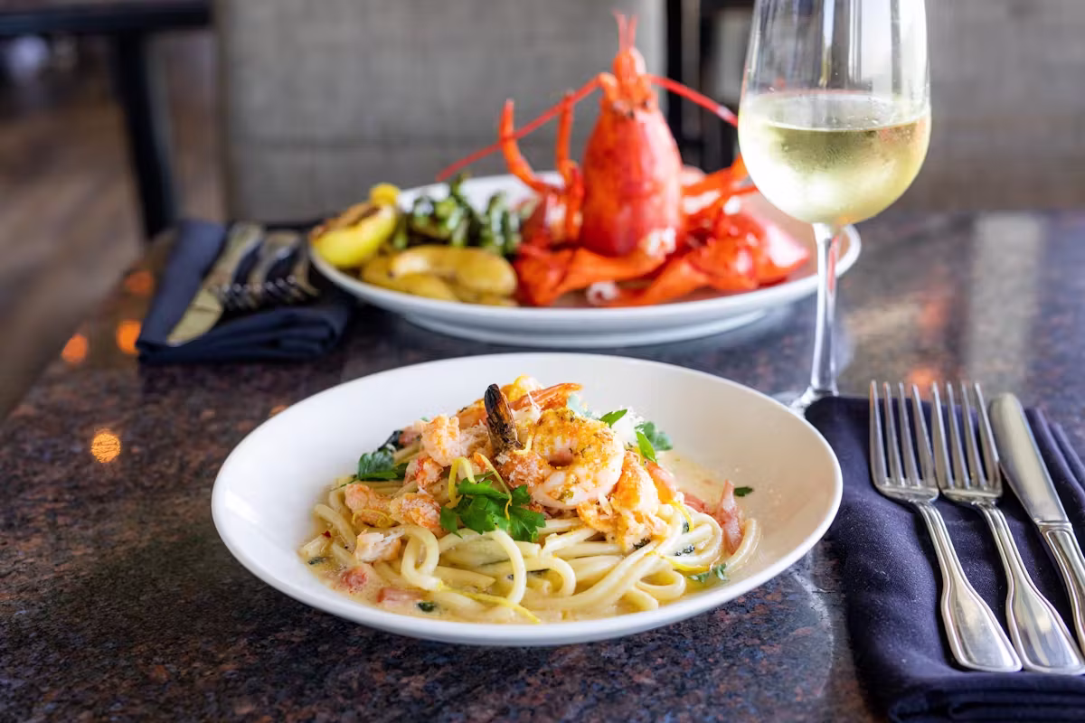 Shrimp pasta, whole lobster, and white wine on a table.