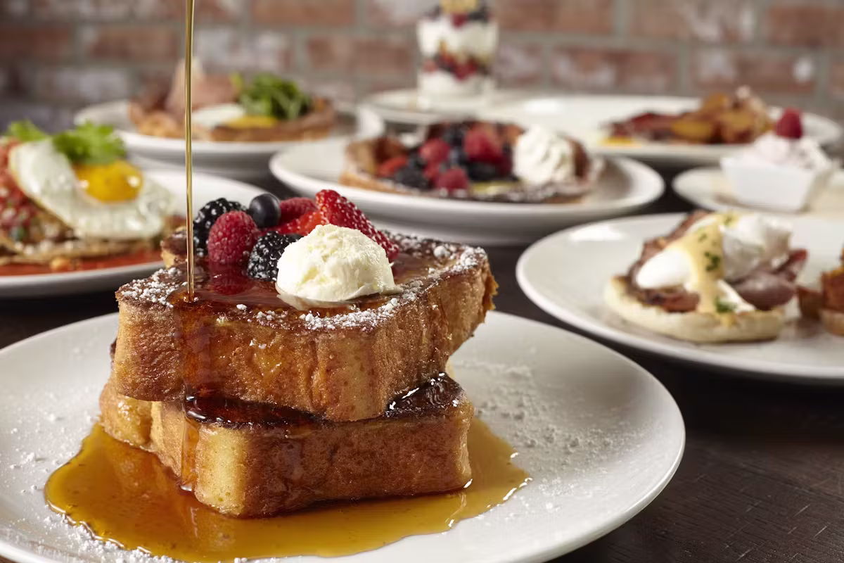 Syrup poured on french toast with berries, cream, and other breakfast items.