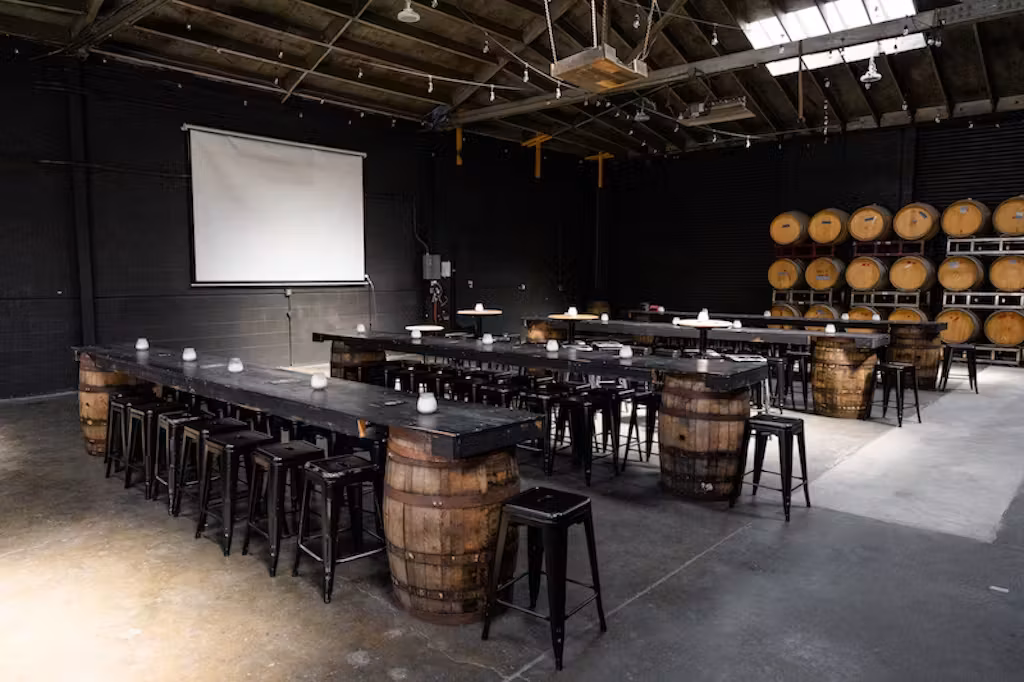 Industrial event space with barrel tables, stools, screen, and stacked barrels.