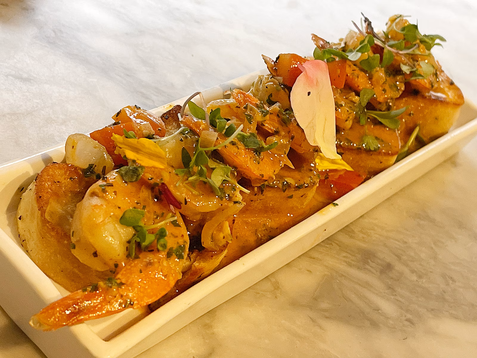 Shrimp and vegetables on toasted bread garnished with herbs and flower petals.