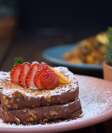 Two slices of French toast with strawberries, orange peel, powdered sugar.