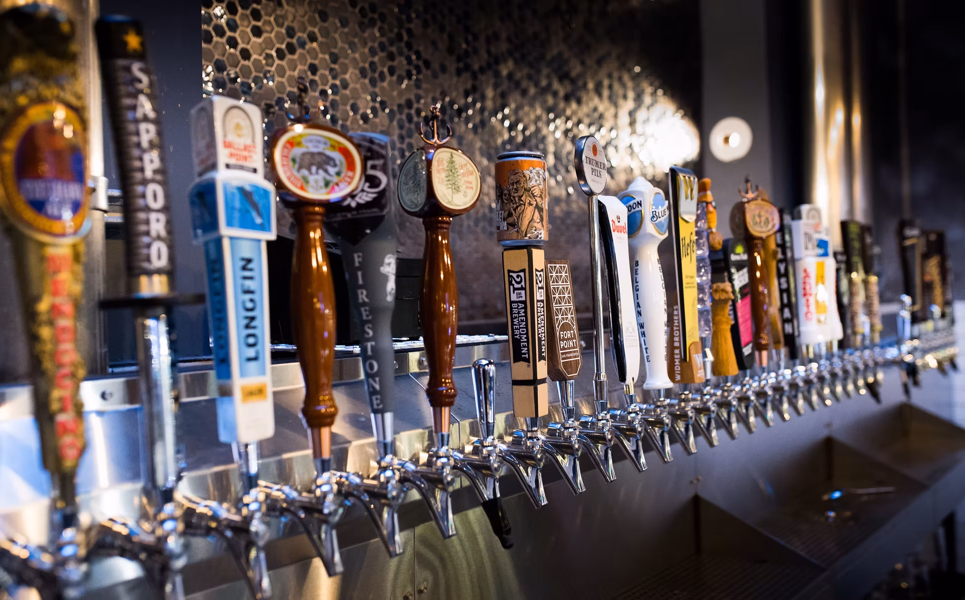A long row of diverse beer tap handles at a bar.