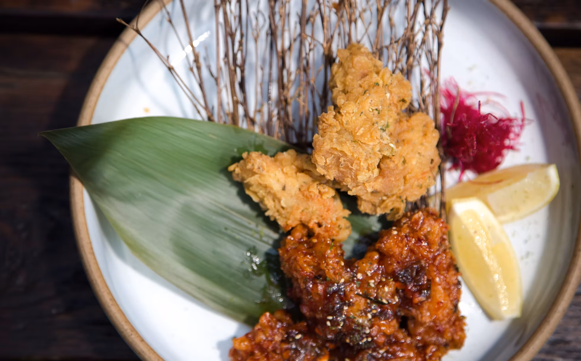 Fried chicken pieces, lemon, green leaf, and twigs on a white plate.