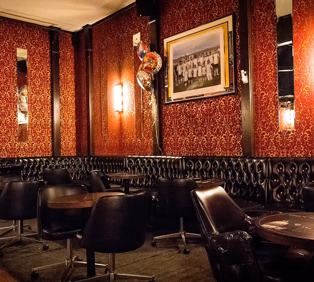 Dimly lit lounge with red wallpaper and dark leather seating.