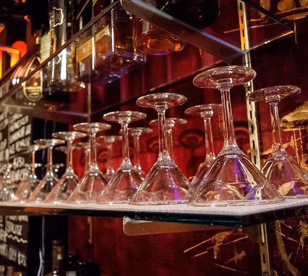 Upside-down martini glasses below liquor bottles on glass shelves.