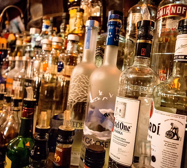 Rows of various liquor bottles, some with pour spouts, in a bar.