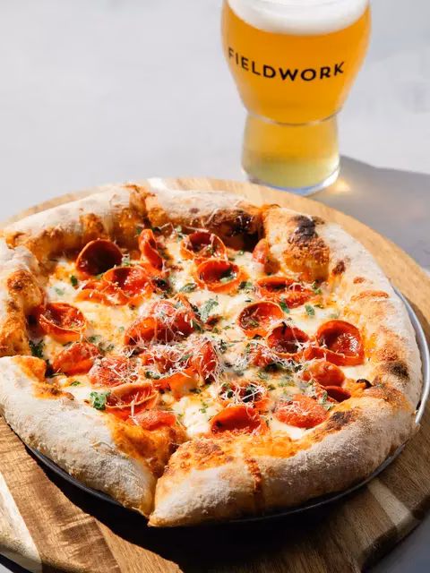 Pepperoni pizza on a wooden board with a Fieldwork beer.