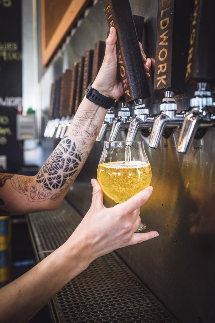 Tattooed arm pulling a Fieldwork beer tap, filling a glass.
